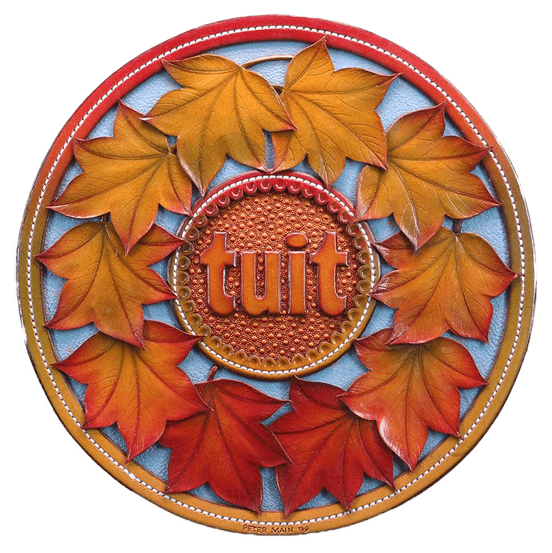 A circular leather piece: a ring of red and orange autumn leaves around a central medallion carved with the word “tuit”.