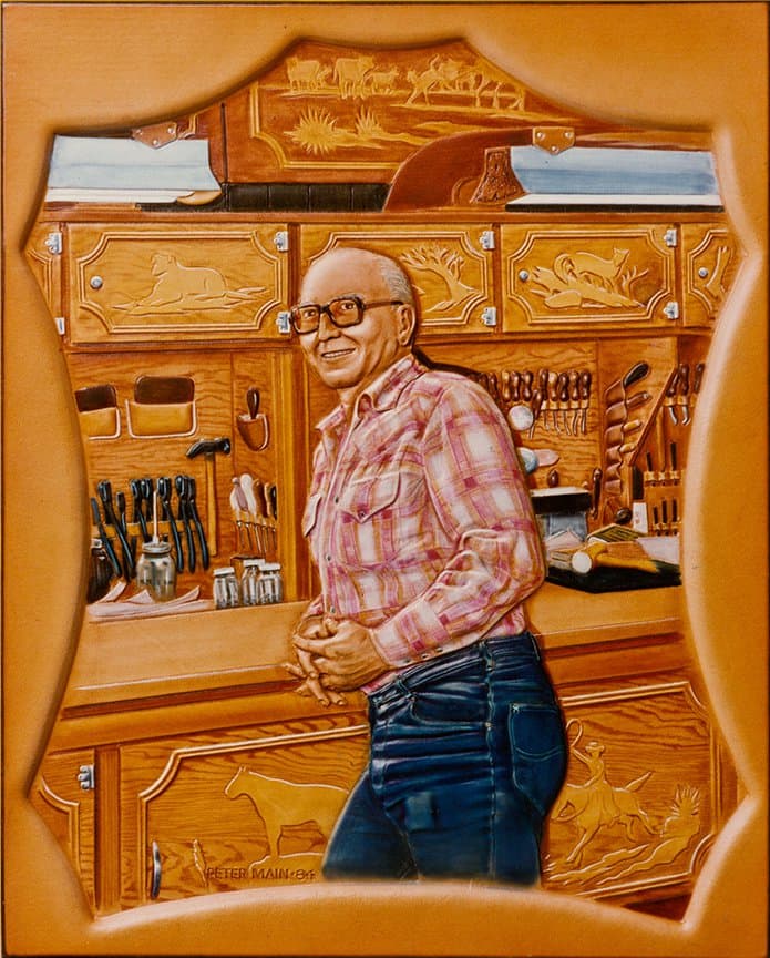 A carved leather portrait of a smiling man in a checked shirt standing in a leatherworking shop, tools on the wall behind him.