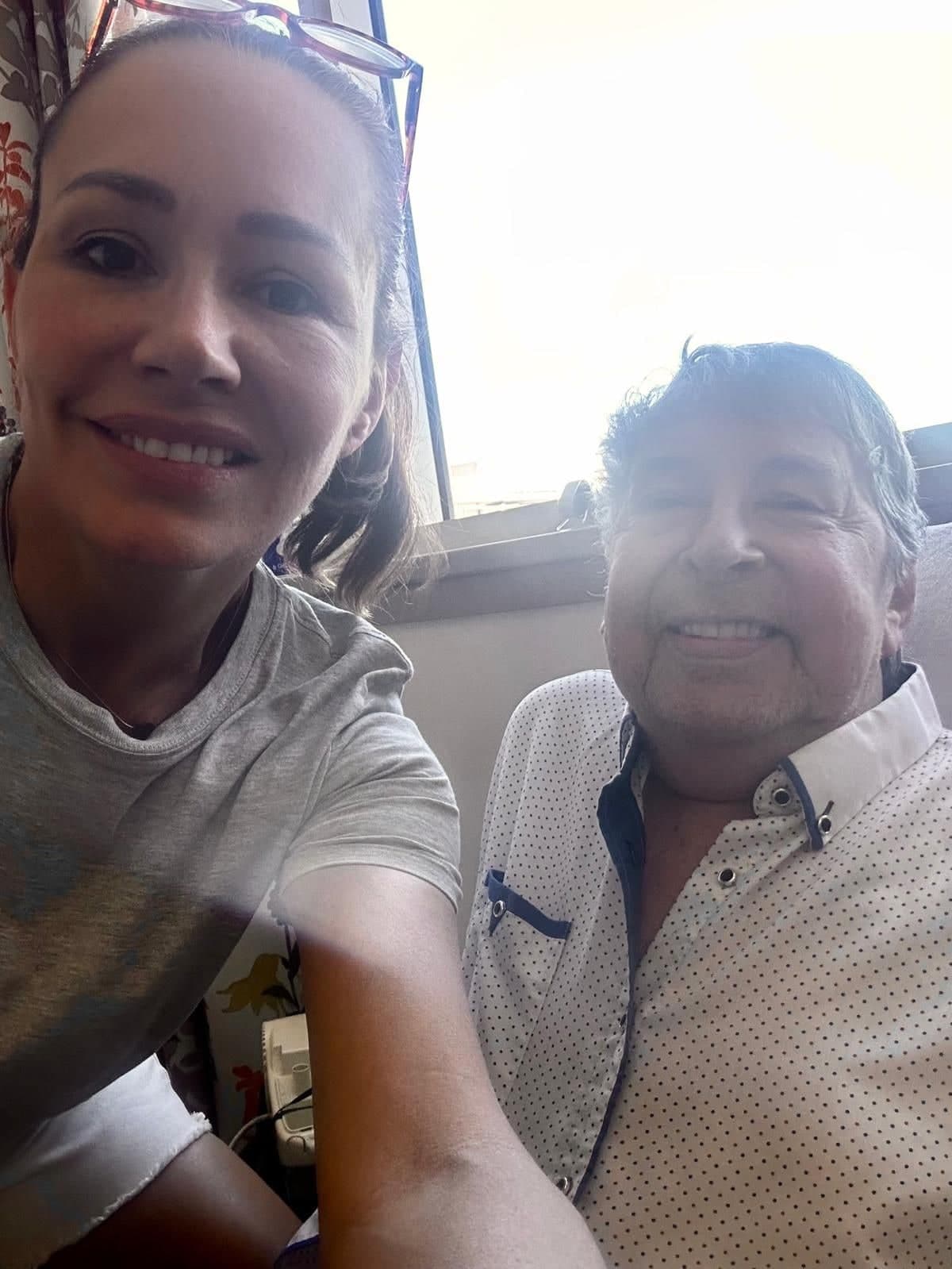 A close photograph of Peter in a white spotted shirt, smiling, his daughter leaning in beside him with sunglasses pushed up into her hair.