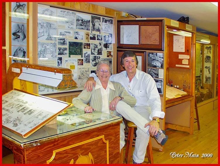 Peter sitting on a stool beside Ann Stohlman in a timber-lined room at the Don King Museum, the walls behind them covered in framed drawings, photographs and leather patterns.
