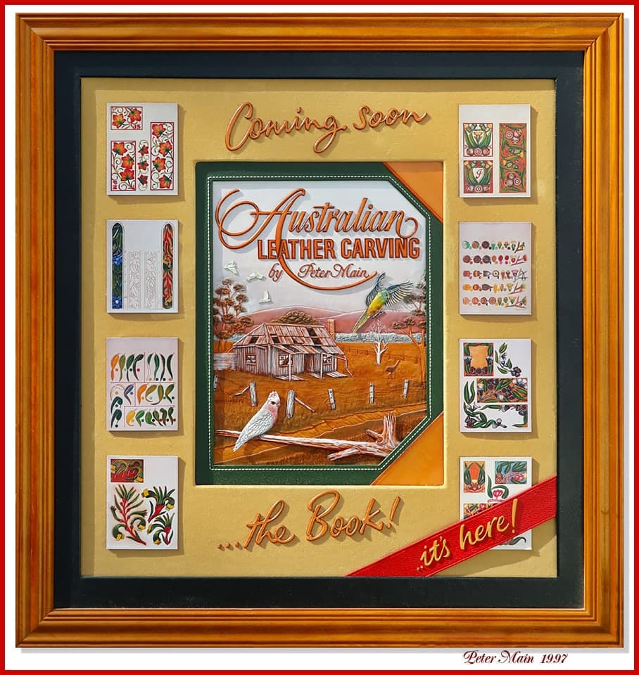 A framed display announcing Australian Leather Carving by Peter Main: the carved and coloured book cover at the centre showing a corrugated-iron farmhouse, a cockatoo and a rosella, surrounded by eight small panels of carved pattern samples, with the words Coming Soon above and a red banner reading it is here.