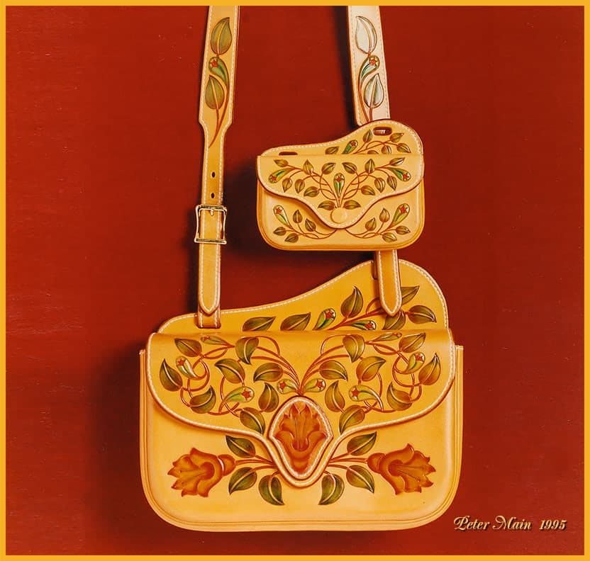 A pale tan shoulder bag and matching purse against a deep red ground, both carved and coloured with fine green leaves, red berries and a tulip at the centre.