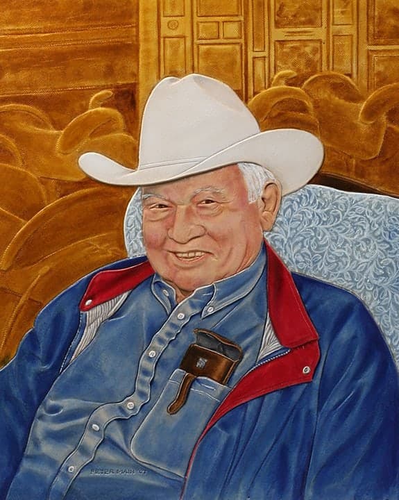 A carved and coloured leather portrait of a smiling older man in a white cowboy hat and a blue jacket with a red collar, sitting in a patterned armchair against a carved gold ground.